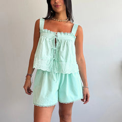 Woman wearing a light green romper with lace details against a plain background