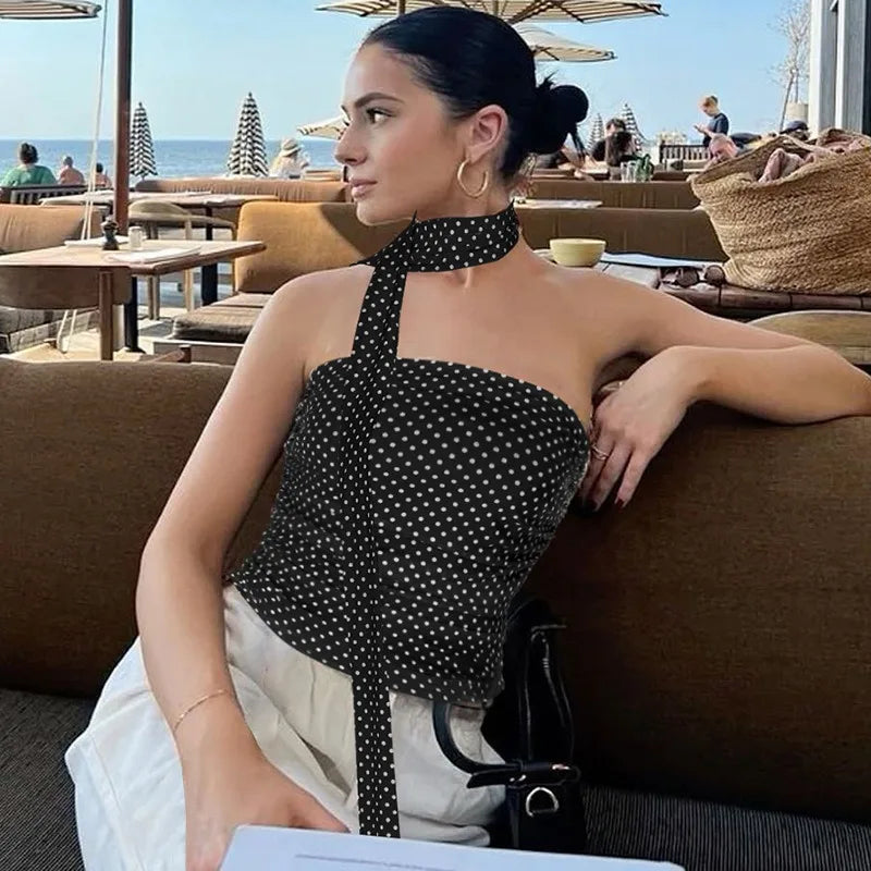 Woman in a polka dot top sitting on a couch with a beachside cafe in the background