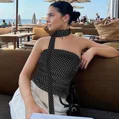 Woman in a polka dot top sitting on a couch with a beachside cafe in the background