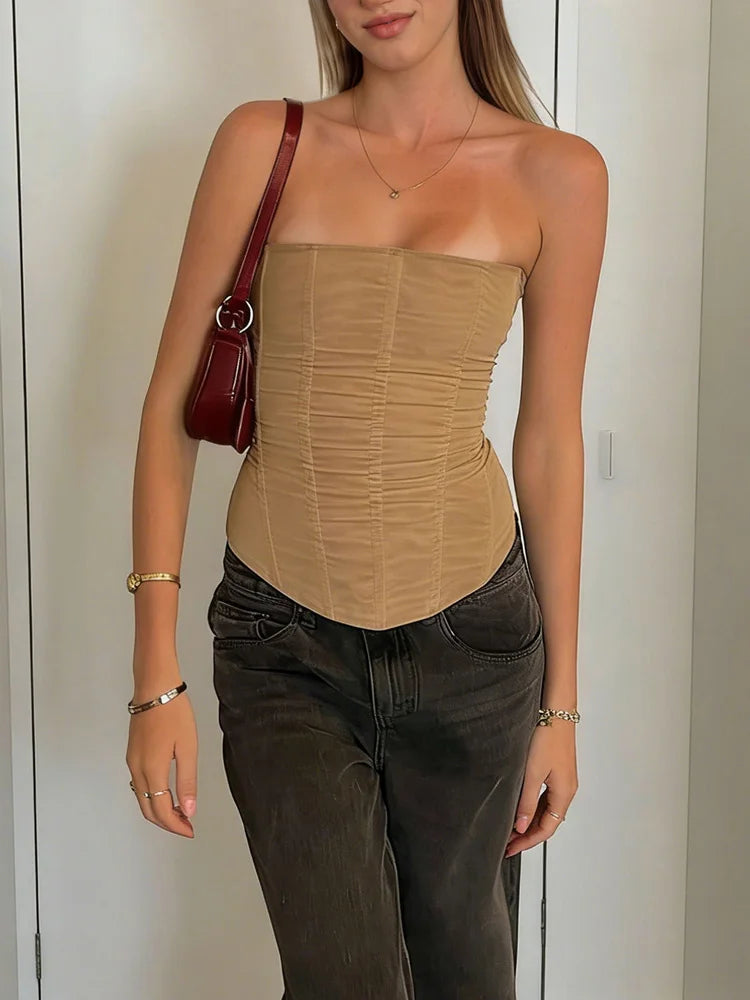 Woman wearing a khaki strapless top and dark jeans, holding a red handbag.