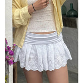 Person wearing a white lace skirt with a yellow jacket and white top, standing against a neutral background.