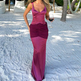 Woman in a long magenta dress holding a glass of red wine on a sandy beach.