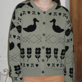 Green cardigan with black floral and duck pattern worn by a person.