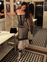 Woman in a vintage-style dress standing in a bathroom with checkered floor and mirror.