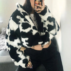 Person wearing a black and white cow print coat, taking a mirror selfie.