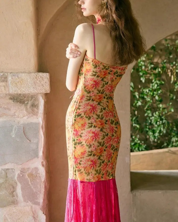 Woman wearing a floral dress with a pink bottom section, standing against a stone wall with greenery.