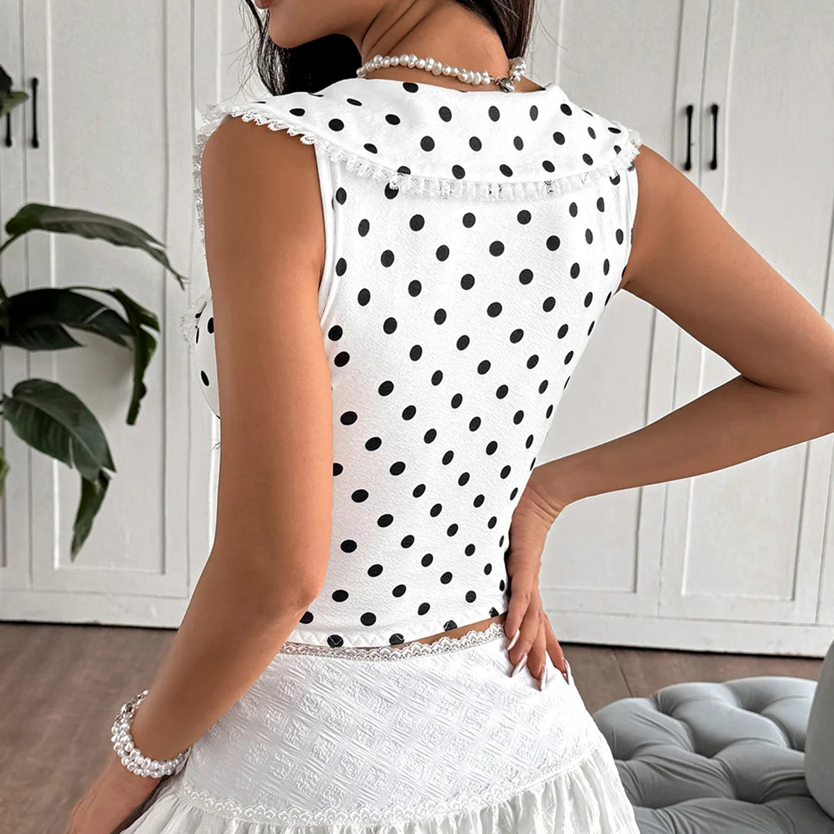 Woman wearing a white sleeveless top with black polka dots and a matching skirt indoors.