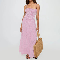 Woman wearing a pink and white striped dress holding a woven bag on a plain background