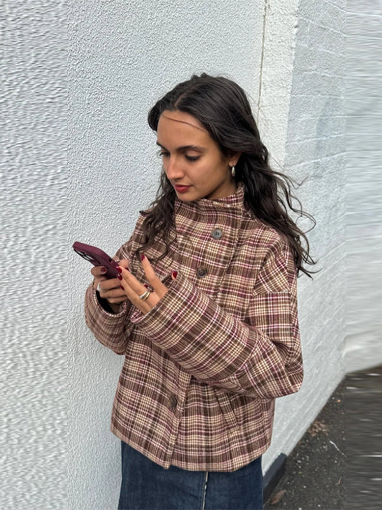 Woman in a plaid jacket looking at her phone against a textured wall.
