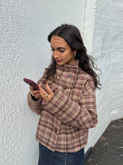 Woman in a plaid jacket looking at her phone against a textured wall.