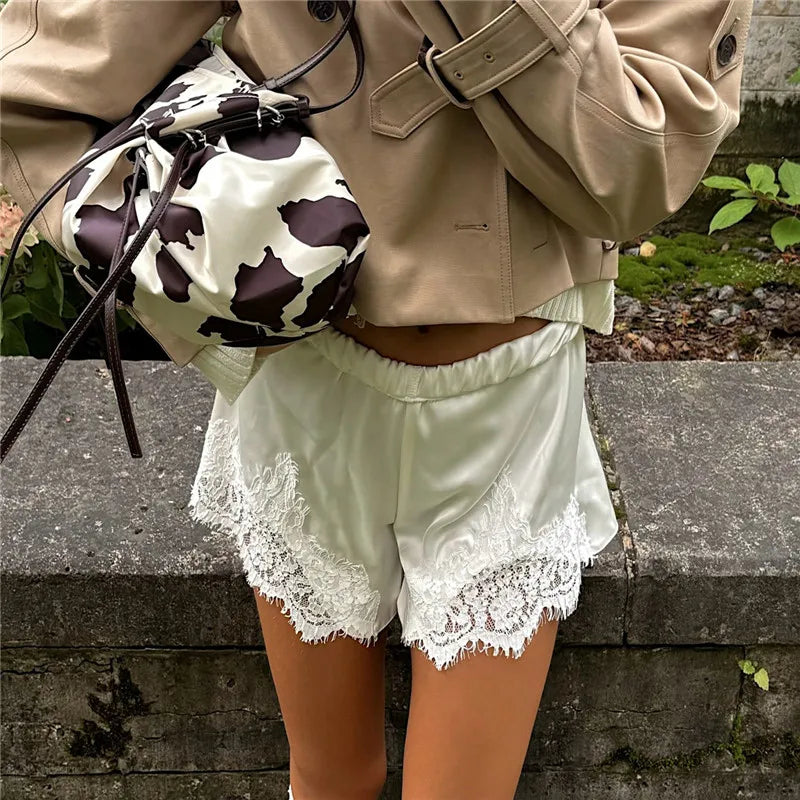 Person wearing a beige jacket and light green shorts with lace trim, holding a cow print bag.