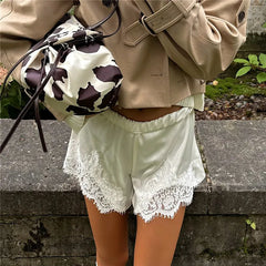 Person wearing a beige jacket and light green shorts with lace trim, holding a cow print bag.