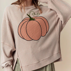 Person wearing a beige sweatshirt with a large pink pumpkin design on a plain background