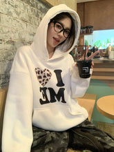 Person wearing a white hoodie with text, sitting indoors holding a drink.