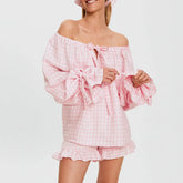 Woman wearing a pink checkered off-shoulder top and shorts set on a white background