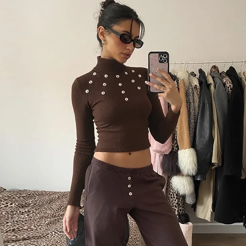 Woman taking a mirror selfie wearing a brown outfit with button details in a room with clothes on a rack.