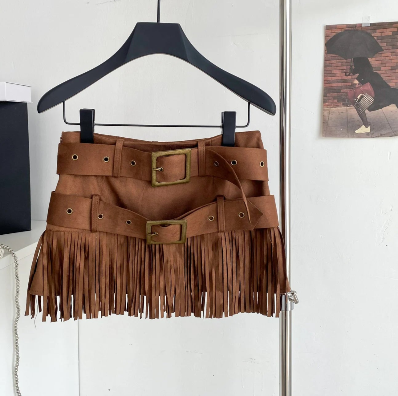 Brown fringe skirt on a hanger with a bag in the background