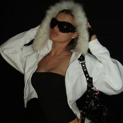 Woman wearing a white fur-lined jacket and black sunglasses against a dark background