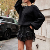Person wearing a black sweater and sequin skirt on a street.