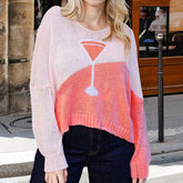 Person wearing a pink and orange sweater with a drink graphic on a city street.