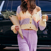 Person wearing a colorful striped sweater and holding a coffee cup and flowers.