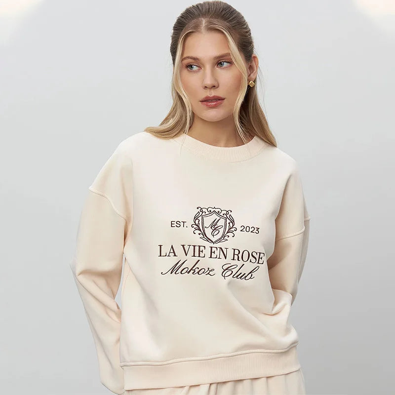 Woman wearing a cream sweatshirt with text and logo on a light gray background