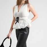 Woman wearing a white sleeveless top with a black ribbon detail on a plain background