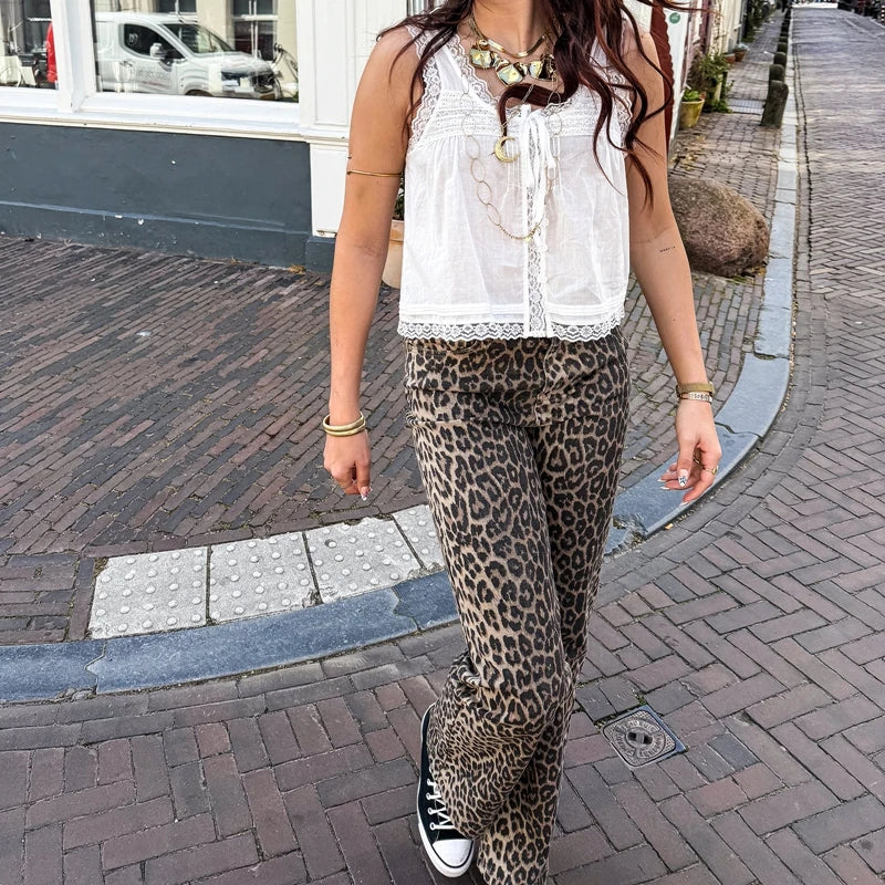 Person wearing a white sleeveless top and leopard print pants on a sidewalk.