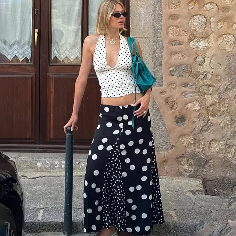 Woman in polka dot top and skirt standing against a stone wall.