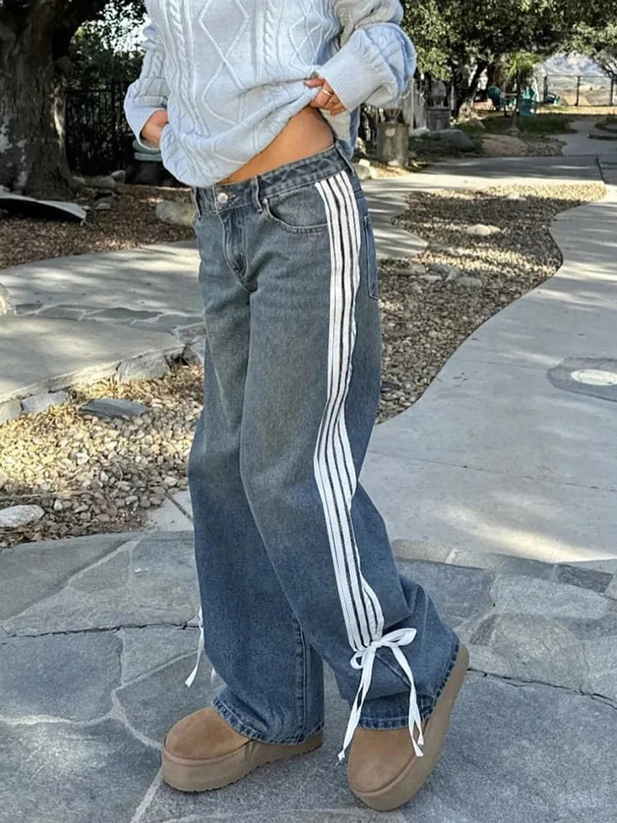 Person wearing blue jeans with white stripes and a light gray sweater outdoors.
