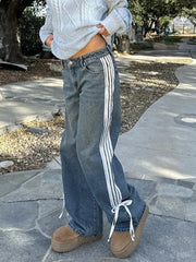 Person wearing blue jeans with white stripes and a light gray sweater outdoors.