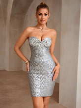 Woman wearing a silver strapless dress with geometric pattern against a neutral background