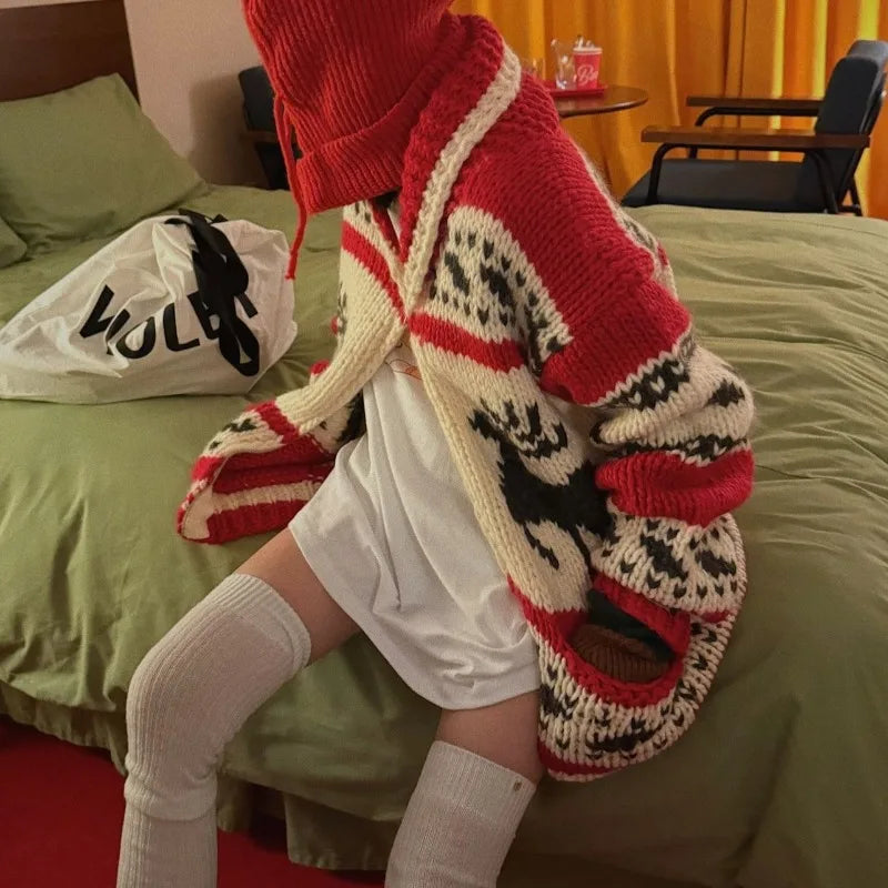 Person wearing a red and white patterned cardigan sitting on a bed in a room.