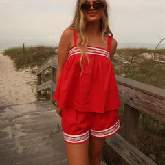 Woman in a red outfit standing on a wooden path near a beach.