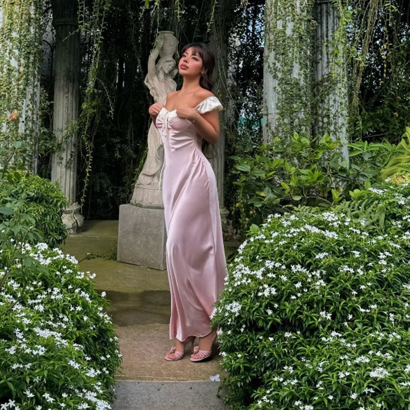 Woman in a pink dress standing in a garden with statues and greenery.