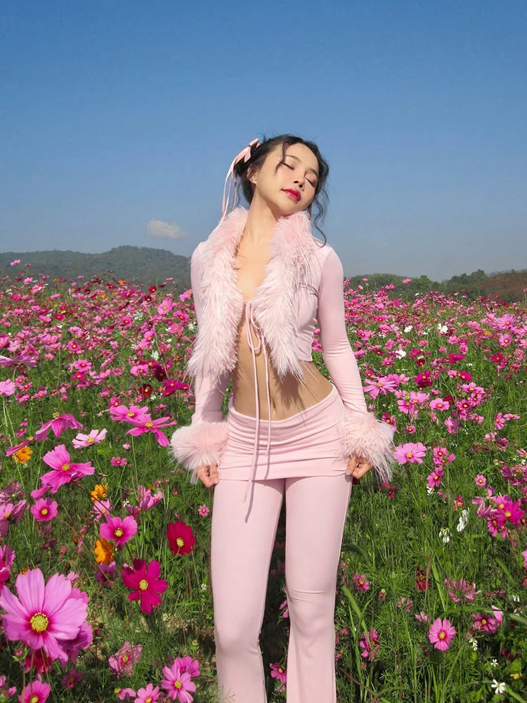 Woman in a pink outfit standing in a field of flowers with a clear blue sky.