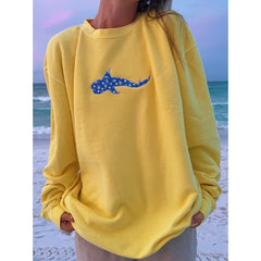 Person wearing a yellow sweatshirt with a blue shark design on a beach