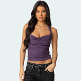Woman wearing a purple halter top and black pants with studs on a light gray background