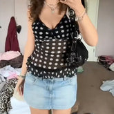 Person wearing a black polka dot top and denim shorts in a room.