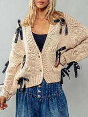 Beige knitted cardigan with black ribbons worn by a person on a gray background