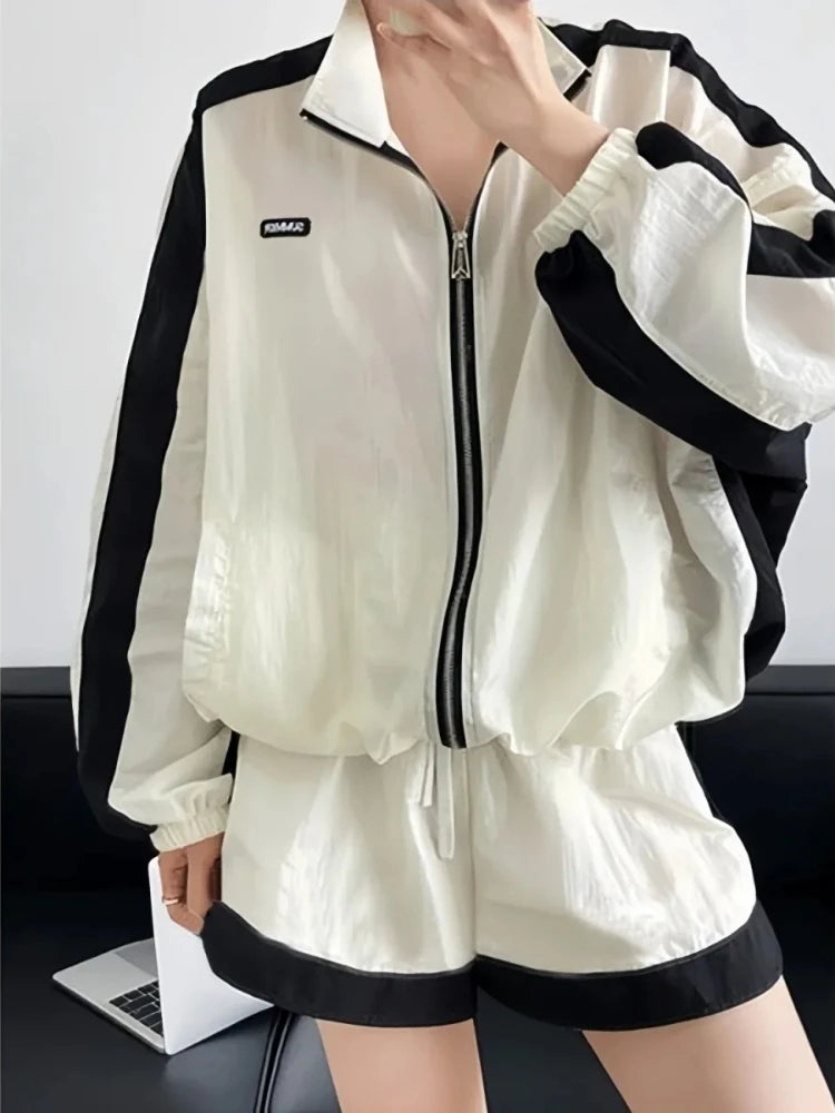 White tracksuit with black accents worn by a person, sitting on a dark surface.