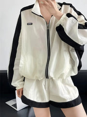 White tracksuit with black accents worn by a person, sitting on a dark surface.