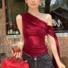 Woman wearing a red one-shoulder top and holding a red handbag and a drink.