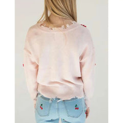 Person wearing a light pink sweater and light blue jeans with cherry embroidery on a plain background