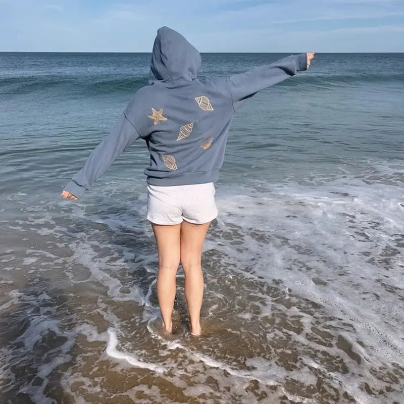 Person wearing a hoodie with shell designs standing in the ocean.