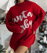 Red sweater with white text worn by a person, Christmas decorations in the background