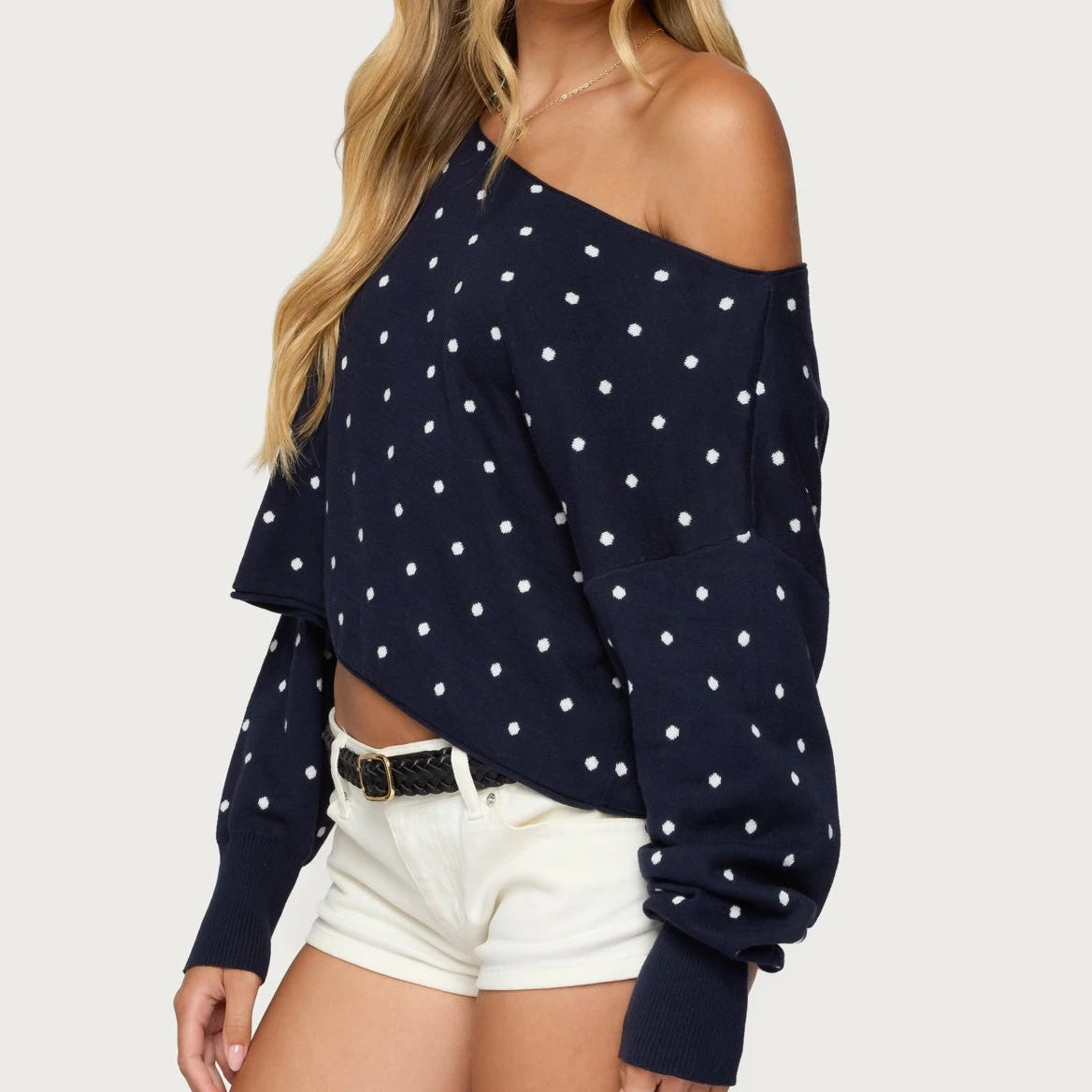 Navy blue off-shoulder top with white polka dots worn by a model on a light gray background