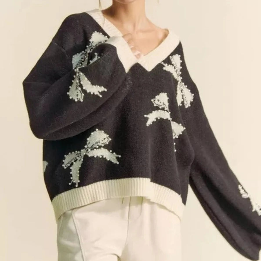 Black sweater with white floral patterns worn by a person on a beige background