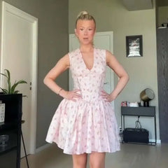 Woman wearing a pink floral dress in a room with a plant and furniture.