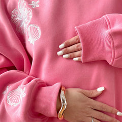 Close-up of a pink sweatshirt with white shell designs and a hand wearing a gold bracelet.